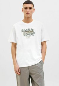 Hvid bomulds t-shirt med grafisk tryk i grå og grøn med teksten "Jack & Jones Originals". T-shirten har en afslappet pasform og korte ærmer.