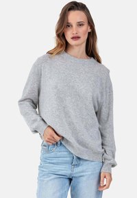 Pull gris en maille avec manches longues, encolure ronde, coupe décontractée et poignets côtelés, associé à un jean bleu clair. Texture douce.