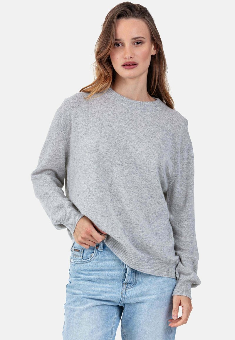 Pull gris en maille avec manches longues, encolure ronde, coupe décontractée et poignets côtelés, associé à un jean bleu clair. Texture douce.