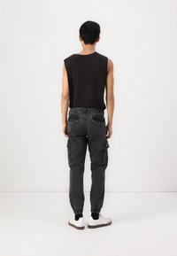 Černý tílko bez rukávů spojené se šedými cargo kalhotami s elastickými manžetami a bočními kapsami. Modelka má na sobě bílé tenisky.