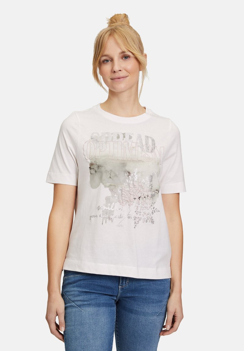 T-shirt bianco in cotone con maniche corte, stampa grafica di fiori e testo "Diffondi Ottimismo", con una leggera consistenza e vestibilità rilassata.