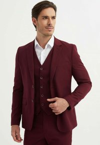 Costume trois pièces bourgogne comprenant un blazer à deux boutons, des revers crantés et un gilet à cinq boutons, associé à une chemise blanche.