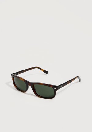 Occhiali da sole a cornice rettangolare in motivo tartarugato con lenti verde scuro e logo Ray-Ban sulle stanghette, posati su una superficie bianca.
