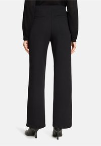 Czarne spodnie o szerokich nogawkach z gładkiej tkaniny, z wysokim stanem, dwoma tylnymi kieszeniami i schludnym wykończeniem nogawek. Połączone z butami na wysokim obcasie.