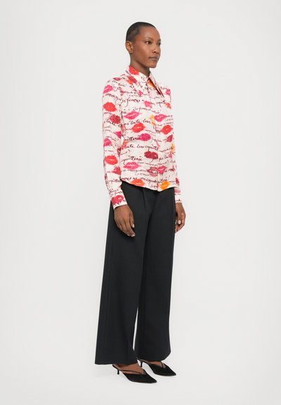 Long-sleeve shirt featuring a white background with red and orange lip prints and black script, paired with wide-leg black pants and black heels.