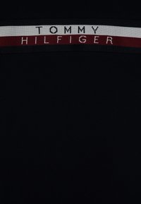 Černé tričko s výrazným vodorovným pruhem v červené, bílé a námořnické modři, na kterém je zobrazeno jméno značky "TOMMY HILFIGER."
