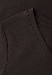 Primer plano de tela marrón oscuro que muestra un cuello en V y una costura en el hombro con puntadas visibles en una camiseta suave de algodón.