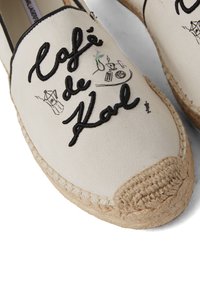 Beige vászon espadrille fekete hímzett "Café de Karl" felirattal és rajzokkal. Fonott juta talppal és lekerekített orral rendelkezik.