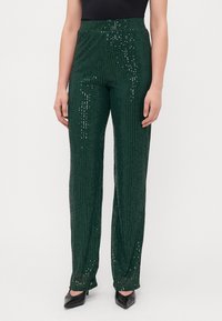 Rohelised sädelevad püksid otse säärekujundusega ja elastse vöökohaga. Kangas on tekstuurse pinnaga ja säravad aktsendid.