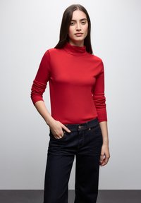 Haut à col roulé rouge à manches longues en matière lisse, associé à un jean en denim foncé avec un design classique à cinq poches.
