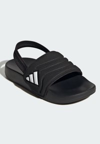 Černé pantofle se strukturovaným páskem a polstrovanou podrážkou. Po straně mají tři bílé pruhy. Vyrobené ze syntetických materiálů.