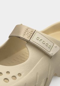 Chaussure Crocs beige avec sangle en tissu ajustable et trous de ventilation au niveau des orteils, vue en gros plan.