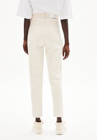 Ljusa beige högmidjade jeans med rak passform, som har två bakfickor och en etikett på den bakre midjebandet. Slät denimtextur.