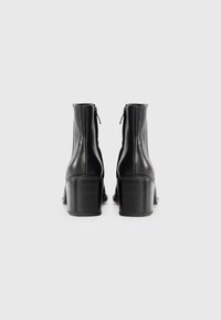 Bocanci negri din piele, la gleznă, cu un finisaj ușor lucios, având tocul pătrat și închidere cu fermoar în spate.