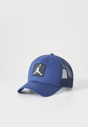 Gorra azul marino con una parte frontal estructurada, parte trasera de malla y un parche negro cuadrado con un logo blanco. Visera curvada con una textura suave.