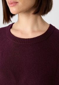 Bordeauxfarbenes Strickpullover mit einem gerippten Rundhalsausschnitt und einer weichen, strukturierten Oberfläche, die eine Nahaufnahme des Kragens und des Halsbereichs zeigt.