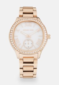 Reloj de pulsera dorado con números romanos, esfera blanca y bisel decorado con cristales. Presenta un pequeño subdial para los segundos. Banda de acero inoxidable.