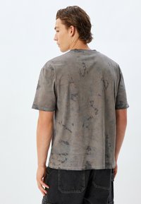 Grå, kortærmet T-shirt med en blød, let slidt tekstur. Har et abstrakt mønster og en standard rund halsudskæring.