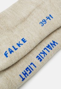 Calzini beige realizzati in morbido materiale, con del testo blu che riporta "FALKE" e "LIGHT" insieme alla taglia "39-41."
