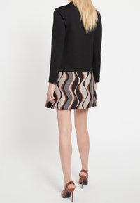 Svart långärmad topp med en vågformad mönstrad kjol i nyanser av beige, svart och orange; ihop med bruna högklackade skor.