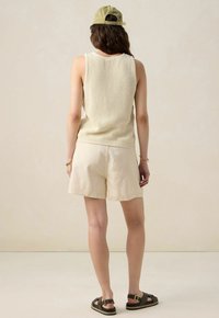 Light beige knit tank top with a textured pattern, paired with cream shorts. Brown strappy sandals complete the outfit. Background is plain.