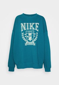 Tealfärgad sweatshirt i bomull, med en stor vit "NIKE"-logotyp, texten 1972 och en skölddesign med lagerbladselement. Långa ärmar.