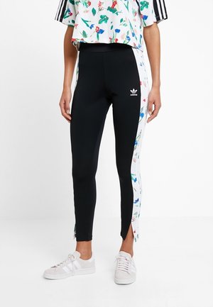 Svarta leggings med vita blommönstrade sidpaneler, elastiskt tyg, figurnära design och sprund vid anklarna. Matchas med en blommig crop top och vita sneakers.