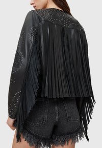 Juoda odinė striukė su kutų detalėmis, smeigtukų puošyba ir trumpintu dizainu. Tekstūruota paviršiaus dalis kontrastuoja su lygiu oda.