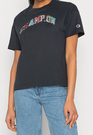 Black cotton t-shirt with short sleeves. Features multi-colored "CHAMPION" embroidered logo across the chest. Fitted design, crew neck.