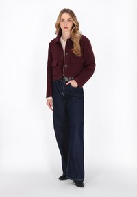 Burgundy kurzes Jacket mit zwei Fronttaschen und Knopfverschluss, kombiniert mit weit geschnittenen marineblauen Jeans und schwarzen Absatzstiefeln.