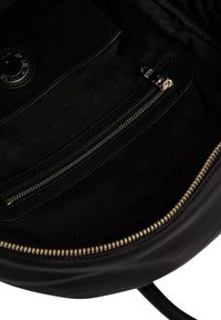 Interior de un bolso de cuero negro con un bolsillo con cremallera y un bolsillo deslizante, que presenta herrajes en tono dorado y un forro de tela suave.