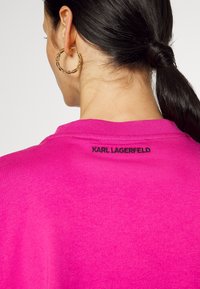Hellrosa Sweatshirt mit Rundhalsausschnitt und einem schwarzen "KARL LAGERFELD"-Logo auf der Rückseite. Der Stoff wirkt weich und glatt.
