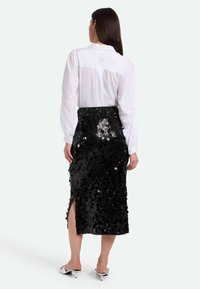 Falda negra de lentejuelas con abertura lateral, combinada con una camiseta blanca de manga larga. Textura suave y superficie brillante con un diseño ajustado.