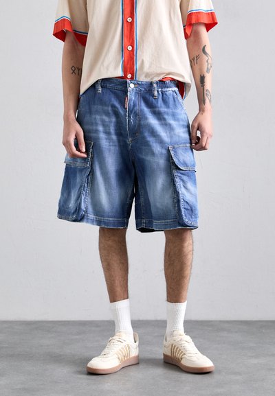 Shorts cargo en denim bleu clair avec deux poches latérales, une coupe décontractée et des détails légèrement distendus. Accompagnés de chaussettes blanches et de baskets.