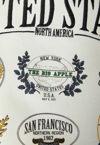 Tekstylna grafika z napisem "Stany Zjednoczone" oraz nazwami miast w czarnych, zielonych i żółtych czcionkach na białym tle, ozdobiona wzorami liści.