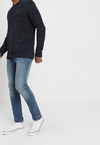 Mörkblå strukturerad stickad tröja med avslappnad passform, kombinerad med ljusblå jeans och vita sneakers. Kännetecknas av enkelhet och komfort.