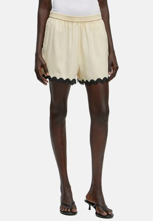 Cremfarbene Shorts mit einem elastischen Bund, die einen schwarzen gewellten Saum am unteren Rand aufweisen. Hergestellt aus einem leichten Stoff.
