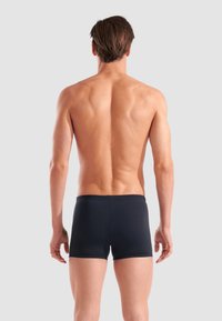 Schwarze Boxershorts aus glattem Material, taillierter Schnitt mit niedrigem Bund. Das Modell wird von hinten betrachtet und zeigt einen minimalistischen Look.
