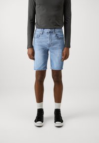 Lyseblå denimshorts med klassisk passform, med høy midje, fem lommer og synlig søm. Kombinert med svarte høyhælte joggesko.