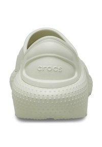White Crocs with a textured rubber exterior, featuring a rounded back and raised dots on the sole. "Crocs" logo embossed on the heel.