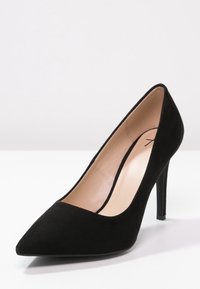 Černá semišová lodička na vysokém podpatku s špičatou špičkou, štíhlým stiletto podpatkem a hladkým béžovým vnitřním podšívkou. Žádné viditelné vzory nebo akcenty.