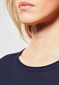 Granatowa, lekka koszulka z okrągłym dekoltem; zbliżenie na szyję i linię szczęki, podkreślające gładką teksturę skóry.
