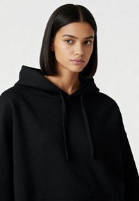 Svart huvtröja gjord av mjukt material. Har en rymlig design med en känguruficka och justerbara snoddar. Slät textur.