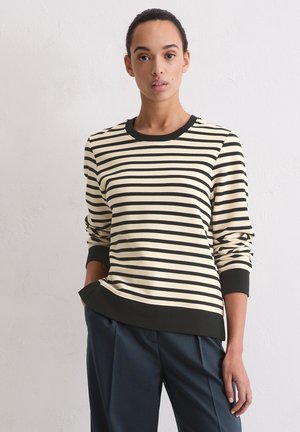 Pull rayé crème et noir avec un col rond, des poignets et un ourlet côtelés. Tissu doux, coupe décontractée et détails de couture visibles.