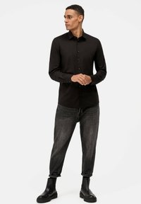 Schwarz langärmliges Hemd mit geknöpften Front, kombiniert mit abgewetzten dunklen Jeans und schwarzen Stiefeletten. Einfaches, elegantes Design.