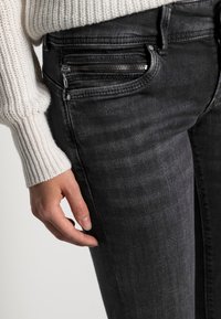 Svarta denimjeans med en slät textur, som har en liten blixtlåsficka, åtsittande design och medelhög midja.