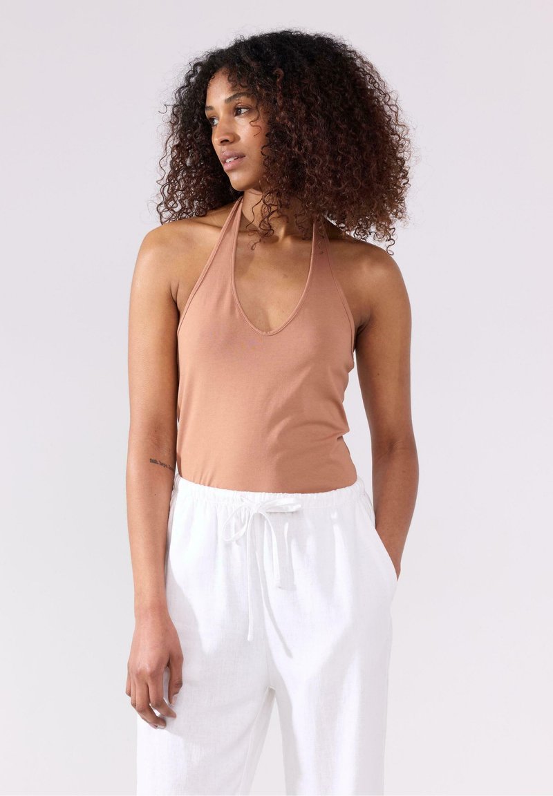 Bruine halter bodysuit met een diepe v-halslijn, gecombineerd met witte joggingsbroek met trekkoord. Glad materiaal met een aansluitend ontwerp en zachte textuur.