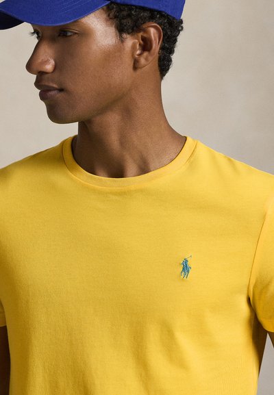 Κίτρινο βαμβακερό t-shirt με στρογγυλή λαιμόκοψη και κοντά μανίκια· διαθέτει μικρό μπλε κεντημένο λογότυπο στο αριστερό στήθος.