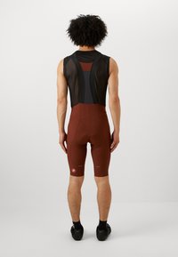 Braune Radsport-Bib-Shorts mit Mesh-Rücken, enganliegende Passform und reflektierenden Details. Sie verfügen über einen gepolsterten Sattel und elastische Beinöffnungen.