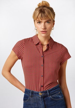 Chemise rouge à manches courtes avec un motif géométrique en crème et bleu. Conception avec boutons sur le devant, col et texture de tissu douce.